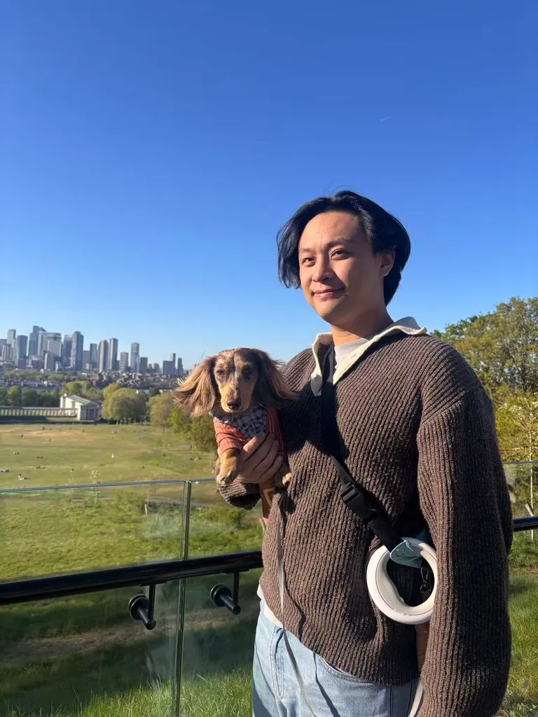 Jason Tang holding a dachshund in front of a city skyline
